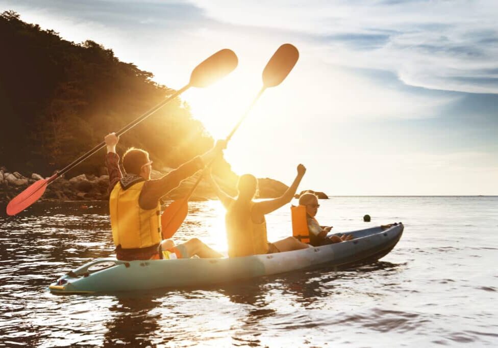 Happy family of father mother and son kayaking and having fun at sunset sea bay